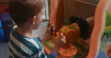 Genç bir çocuk oyun merkezinde interaktif bir oyun oynuyor. Çocuk, renkli denetimler ve etkinlikler içeren, eğlence ve öğrenmeyi teşvik eden oyuna odaklanmış durumda..