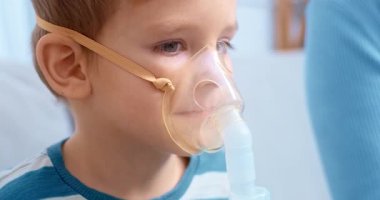 Nebulizör maskesi takan küçük bir çocuk evde solunum tedavisi görüyor. Çocuk sakin görünüyor ve oturuyor. Çocuklar için solunum tedavisinin önemini vurguluyor..
