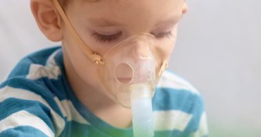 Çizgili gömlek giyen genç bir çocuk solunum tedavisi için nebulizör kullanır. Sahne, ev sağlığı ve pediatrik solunum hizmetlerinin önemini yansıtıyor..