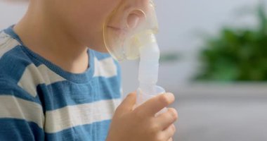 Çizgili gömlekli bir çocuk solunum terapisi için nebulizör kullanıyor. Sahne, rahat bir ortamda ev sağlığı ve pediatrik solunum hizmetlerini vurguluyor.