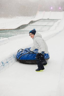 Kışın giyinmiş bir çocuk karlı bir yamaçtan aşağıya kar tüpü ile inmeye hazırlanıyor. Sahne, kar tanelerinin arasında kış aktivitelerinin heyecanını ve eğlencesini yakalıyor..