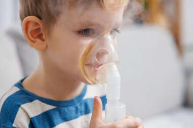 Küçük bir çocuk solunum terapisi için nebulizör maskesi kullanıyor, solunum sorunlarını tedavi etmek için ilaç soluyor. Olay yeri, pediatrik bakım odaklı bir ev sağlığı seti yakalıyor..