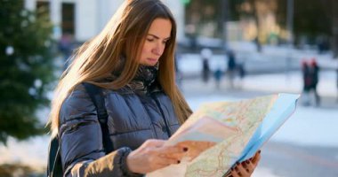 Kışlık ceketli bir kadın şehir ortamında bir haritayı inceliyor. Sahne, karlı bir şehirde yol alırken onun dikkatini ve kararlılığını çekiyor..