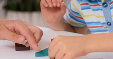 Beyaz bir masanın üzerinde renkli tahta bloklar düzenleyen iki insanın yakın çekim sekansı. Etkileşim, öğrenme, takım çalışması veya eğitim kavramları için uygun rehberlik ya da işbirlikçi oyun önerir.