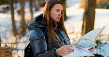 Kışlık ceketli bir kadın, karlı bir ormanda harita çalışıyor. Sahne, dingin ve soğuk ortamda gezinirken onun odaklanmış yüz ifadesini yakalıyor. Keşif ve macerayı ön plana çıkarıyor..