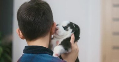 Genç bir çocuk, küçük siyah beyaz bir köpek yavrusuyla nazikçe kucaklaşıp etkileşime girerken görülüyor. Video, çocukluk arkadaşlığı ve evcil hayvan bakımı kavramını gösteren hassas bir anı yakalıyor..