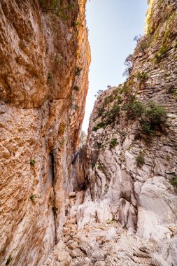 Geçide bakan bir perspektif, yakın kaya duvarının pürüzlü, dokulu yüzeyini ve dar geçide doğru giden gevşek kayaların yolunu vurguluyor..