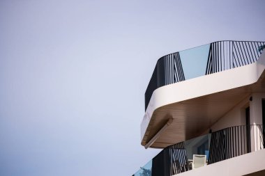 Düşük açılı, kıvrımlı, yeni beyaz bir apartmanın çağdaş balkonlarının temiz gökyüzüne karşı siyah ve cam korkulukların olduğu yakın çekim..