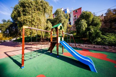 Üzerinde mavi bir kaydırak ve tırmanma çerçevesi olan canlı bir oyun alanı. Arka planda Villajoyosa 'nın çok renkli evleri var..