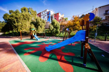 Mavi kaydırak ve yeşil ve kırmızı güvenlik zeminli parlak bir oyun alanı, tarihi bölgenin geleneksel renkli binaları tarafından gözden kaçırıldı..