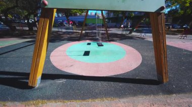 Benidorm, İspanya 'da renkli bir şehir parkında, parlak mavi gökyüzünün altında yavaşça sallanan tek bir boş salıncağın alçak açılı çekimi..