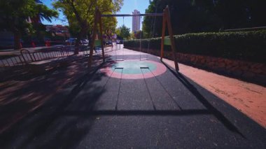 Benidorm, Alicante, Spain.2026-02-19.Çift salıncaklı mükemmel bir çekim, oyun parkı zeminindeki renkli dairesel desenleri ve parkın yeşilliği tarafından çerçevelenmiş uzak bir gökdeleni gösteriyor..