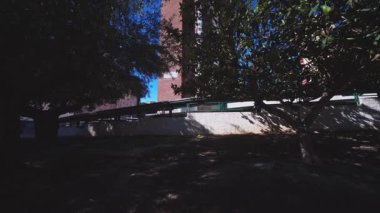 Akdeniz çam ve yaprak döken ağaçların kalın dalları ve yapraklarıyla çerçevelenmiş uzun tuğla renkli bir binaya bakan dramatik alçak açılı bir çekim..