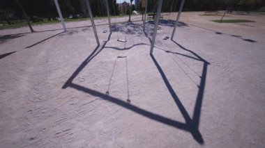 Benidorm parkındaki modern bir salıncak yapısının geniş açılı görüntüsü, açık mavi gökyüzünün altında kumların üzerine dökülen uzun gölgeler..