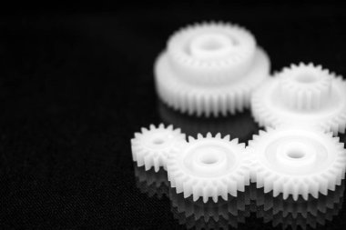 Siyah ayna arka planında birkaç beyaz plastik dişli. Mekanik onarım. Düzelt. Yansıma. Tamirci. Çarklar. Büyük bir mekanizmanın elementleri. Uyumlu bir çalışma. İş başarısı. Bulanık arkaplan.