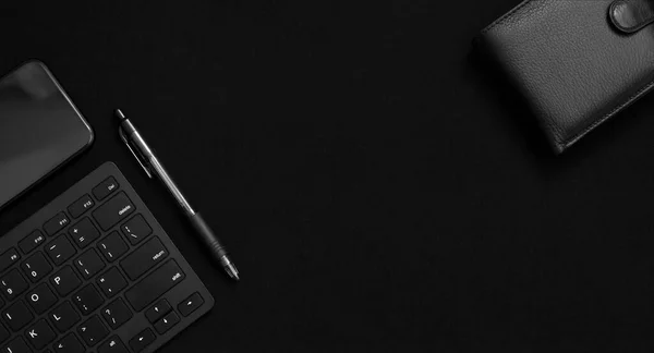 Flat lay composition with black pen, computer keyboard, smartphone and leather wallet on dark black surface. Business concept. Business people items. Free space for text. Low key photo. Stationery. Items of successful people.