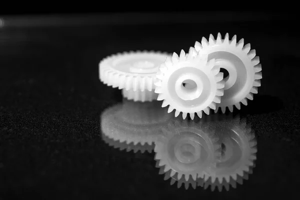 Several white plastic gears on a black mirror background. Mechanical repair. Fix. Reflection. Repair shop. Cogwheels. Elements of a large mechanism. Harmonious work. Business success. Blurred background.