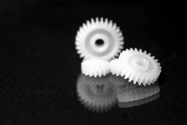 Several white plastic gears on a black mirror background. Mechanical repair. Fix. Reflection. Repair shop. Cogwheels. Elements of a large mechanism. Harmonious work. Business success. Blurred background.