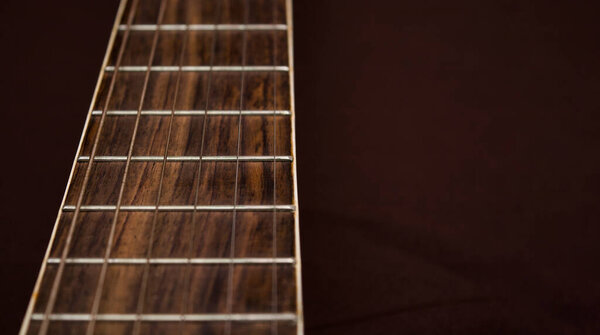 Neck of the guitar close-up. Strings and frets on the neck of the guitar. Musical instrument on a brown background.