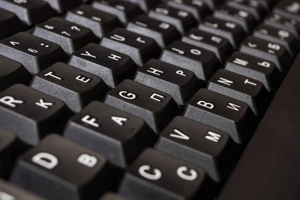 Black Computer keyboard buttons with English and Russian letters closeup.