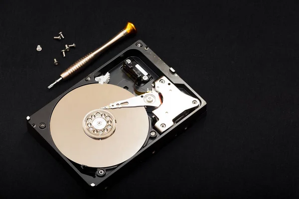 Internal parts of the hard drive. HDD. Computer memory. Modern technologies. Computer repair. Data storage concept. Black background. Free space for text. Recover lost data. Screwdriver and bolts near the hard drive.