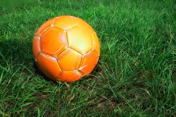 Old Orange soccer ball on green grass. The concept of street football. An old ball with cracks. Healthy lifestyle. Sport. Victory.