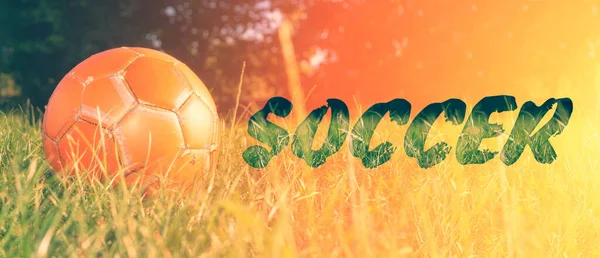 Orange soccer ball on green grass. The concept of street football. An old ball with cracks. Healthy lifestyle. Sport. Victory. The inscription is soccer.