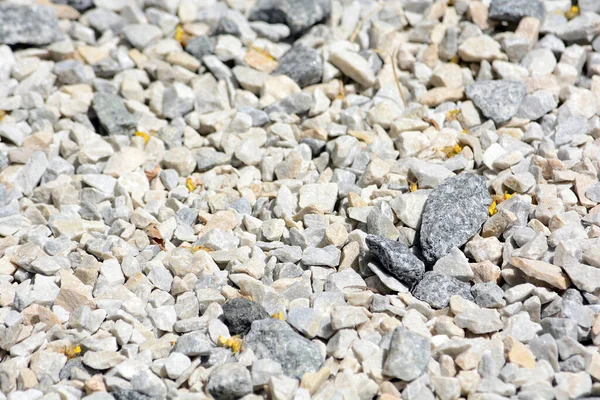 small rock crushed stone road-metal. Gravel is a type of rock. Pile of white, grey and yellow rocks. Road-metal background.