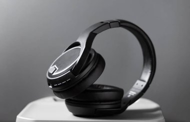 Gri arka planda modern siyah kablosuz kulaklıklar. Müzik, ses ve teknoloji kavramları için üst kulaklı bir cihaz. Reklam, tasarım veya sosyal medya kullanımı için minimalist kompozisyon.