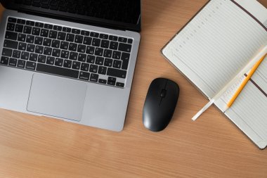 Dizüstü bilgisayarı, bilgisayar faresi, açık not defteri ve sarı kalemi olan bir masanın üst görüntüsü. Uzak çalışma, öğrenim, planlama ve modern verimlilik için rahat ofis kurulumu.