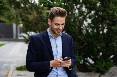 Akıllı telefon kullanan ve gülümseyen yakışıklı bir iş adamı. Mutlu genç adam cep telefonu uygulamaları kullanıyor, mesaj atıyor, internette geziniyor, akıllı telefona bakıyor. Mobil aygıtlarla çalışan gençler