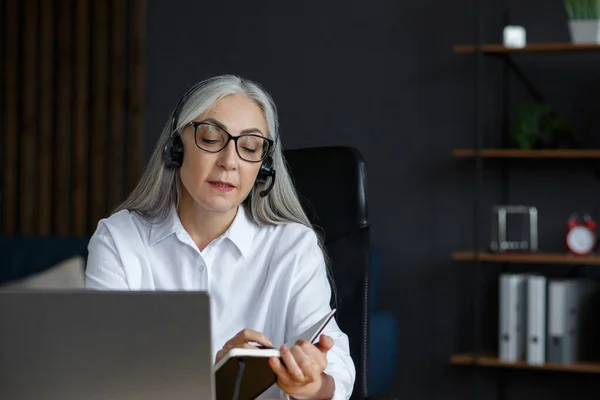 Retrato de una hermosa anciana sonriente que estudia en línea. Educación en línea, trabajo a distancia, educación en el hogar. Mujer mayor de cabello gris escribiendo en cuaderno. Las personas maduras estudian cursos en línea — Foto de Stock