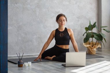 Genç, sportif kadın yoga eğitmeni çevrimiçi koçluk yapıyor. Laptop kamerasında yoga dersleri videosu çekiyor. Yoga pozu veren güzel bir kadın. Yoga duruşu, meditasyon, rahatlama, refah ve sağlık