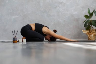 Evde yoga dersi veren sportif genç bir kadının portresi. Çocuk yogası pozu veren güzel bir kız, Balasana. Yoga duruşları, meditasyon, rahatlama, stres yönetimi, refah ve sağlık