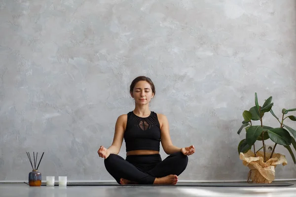 Portrait of sporty young woman doing exercises on yoga lesson at home. Beautiful girl practicing easy yoga pose, sukhasana. Yoga postures,meditation,relaxation,stress management, wellbeing and health