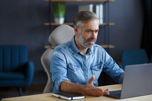 Portrait of grey-haired senior handsome smiling man working from home. Communication online with colleagues and video conference. Online meeting, video call, remote working