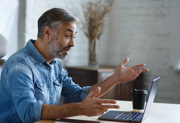 Portrait of grey-haired senior handsome smiling man working from home. Communication online with colleagues and video conference. Online meeting, video call, remote working