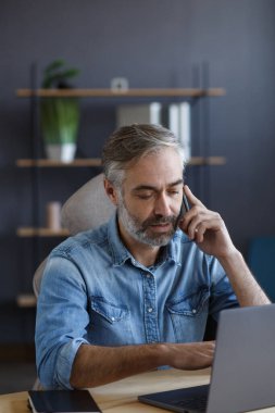 Kıdemli gri saçlı işadamı ofiste telefonla konuşuyor. İş ortaklarıyla sohbet. İş yerinde oturan yakışıklı olgun bir adamın iş portresi. İletişim, müzakere