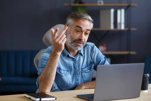 Retrato de un hombre mayor de pelo gris, guapo y sonriente que trabaja desde casa. Comunicación en línea con colegas y videoconferencia. Reunión en línea, videollamada, trabajo remoto — Foto de Stock