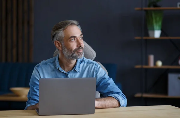 Hombre mayor de pelo gris que trabaja en la oficina del hogar con portátil. Retrato de negocios del gerente guapo sentado en el lugar de trabajo. Estudiar en línea, cursos en línea. Concepto empresarial —  Fotos de Stock