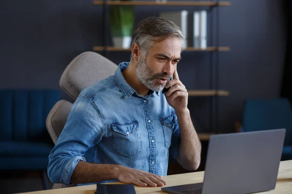 Un hombre de negocios de pelo gris hablando por teléfono en la oficina. Conversación con socios comerciales. Retrato de negocios del guapo hombre maduro sentado en el lugar de trabajo. Comunicación, negociación — Foto de Stock