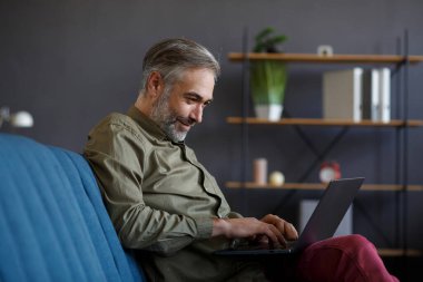 Merkez ofiste dizüstü bilgisayarla çalışan kıdemli bir adam. Kanepede oturan yakışıklı gri saçlı müdürün portresi. Çevrimiçi, çevrimiçi kurslar. Çevrimiçi eğitim, uzaktan çalışma