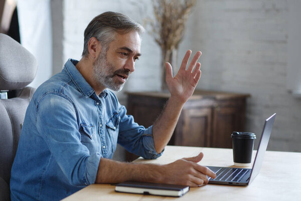 Portrait of grey-haired senior handsome smiling man working from home. Communication online with colleagues and video conference. Online meeting, video call, remote working