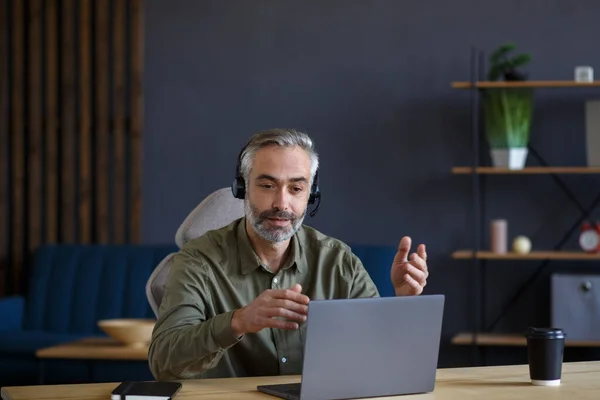 Retrato de un hombre guapo mayor de pelo gris enseñando en línea. Educación en línea, trabajo a distancia, educación en el hogar. Reunión en línea, videollamada, videoconferencia, cursos en línea —  Fotos de Stock