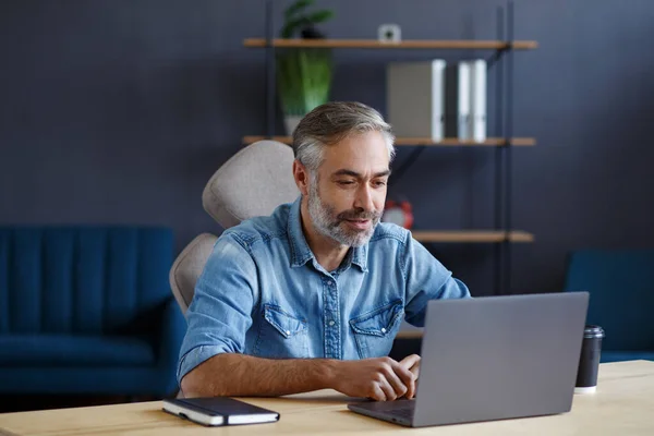 Retrato de un hombre mayor de pelo gris, guapo y sonriente que trabaja desde casa. Comunicación en línea con colegas y videoconferencia. Reunión en línea, videollamada, trabajo remoto — Foto de Stock