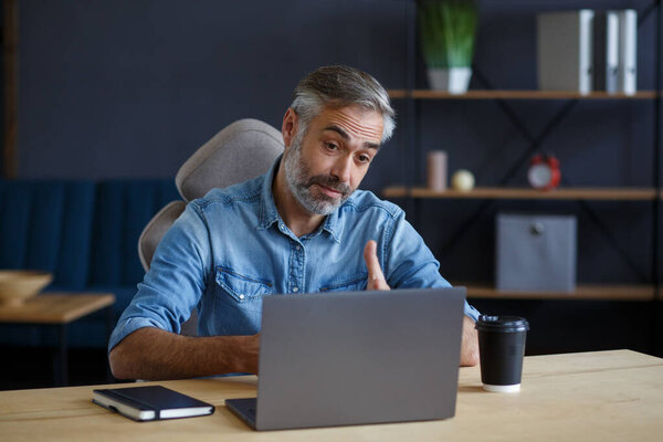 Portrait of grey-haired senior handsome smiling man working from home. Communication online with colleagues and video conference. Online meeting, video call, remote working