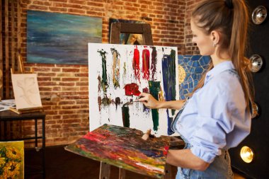 Stüdyodaki ressam yağlı boya tabloları ve palet bıçağıyla tuvalde soyut bir resim oluşturuyor. Çalışan genç bir kadın sanatçı. Yaratıcı süreç, rahatlama, rahatlama, hobi, stres yönetimi.