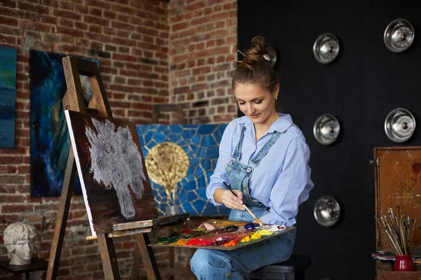 Young beautiful female artist painting still life with sunflower on canvas using oil paintings and art brush. Painter creating artwork in art studio. Relaxation, leisure, hobby, stress management