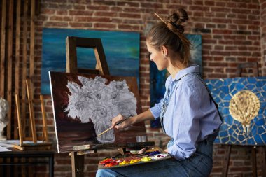 Genç ve güzel kadın ressam, yağlı boya tabloları ve sanat fırçasıyla tuval üzerinde ayçiçeğiyle resim yapıyor. Ressam sanat stüdyosunda sanat eseri yaratıyor. Rahatlama, rahatlama, hobi, stres yönetimi