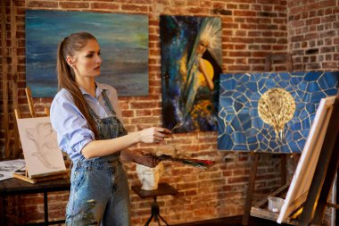 Yağlı boya tabloları ve sanat fırçasıyla tuvale resim yapan genç ve güzel bir kadın sanatçı. Ressam sanat stüdyosunda sanat eseri yaratıyor. Rahatlama, rahatlama, hobi, stres yönetimi